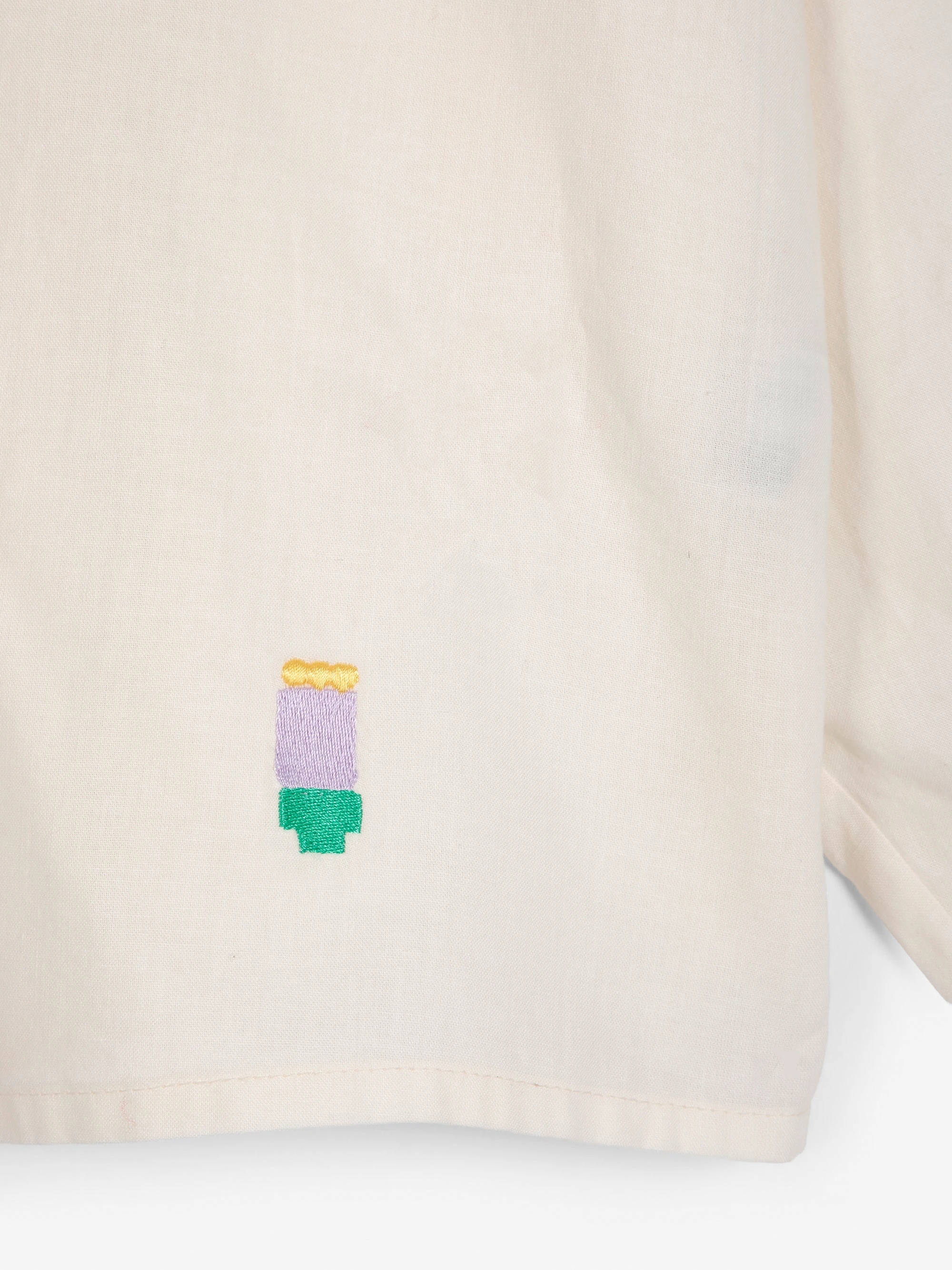 Original cream shirt product photo showing the bottom hem and small multicolor embroidered detail